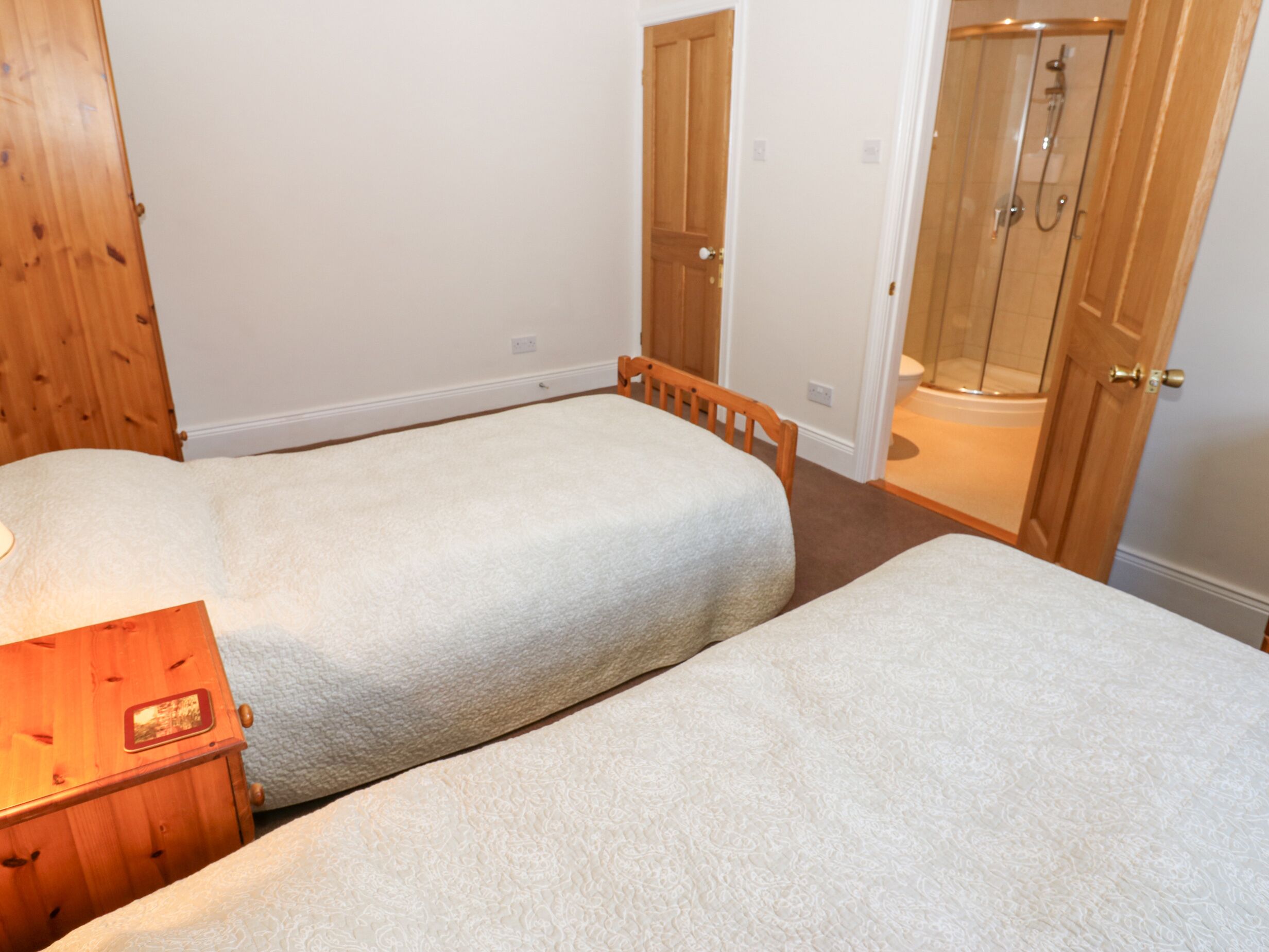 A bedroom with two single beds, a wooden dresser, and a shower area.