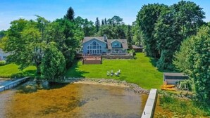 Een groot huis met een vijver op de voorgrond, omgeven door weelderige begroeiing.