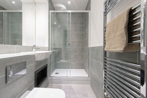 Une salle de bain moderne avec une douche à parois de verre, un grand miroir, un lavabo blanc et un porte-serviettes.