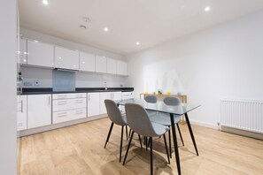 Une cuisine moderne avec des meubles blancs, un plan de travail noir et une table à manger en verre, assortie de chaises.