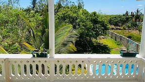 A covered balcony with a view of a lush garden and palm trees. - Silent Palms (Diani Beach)