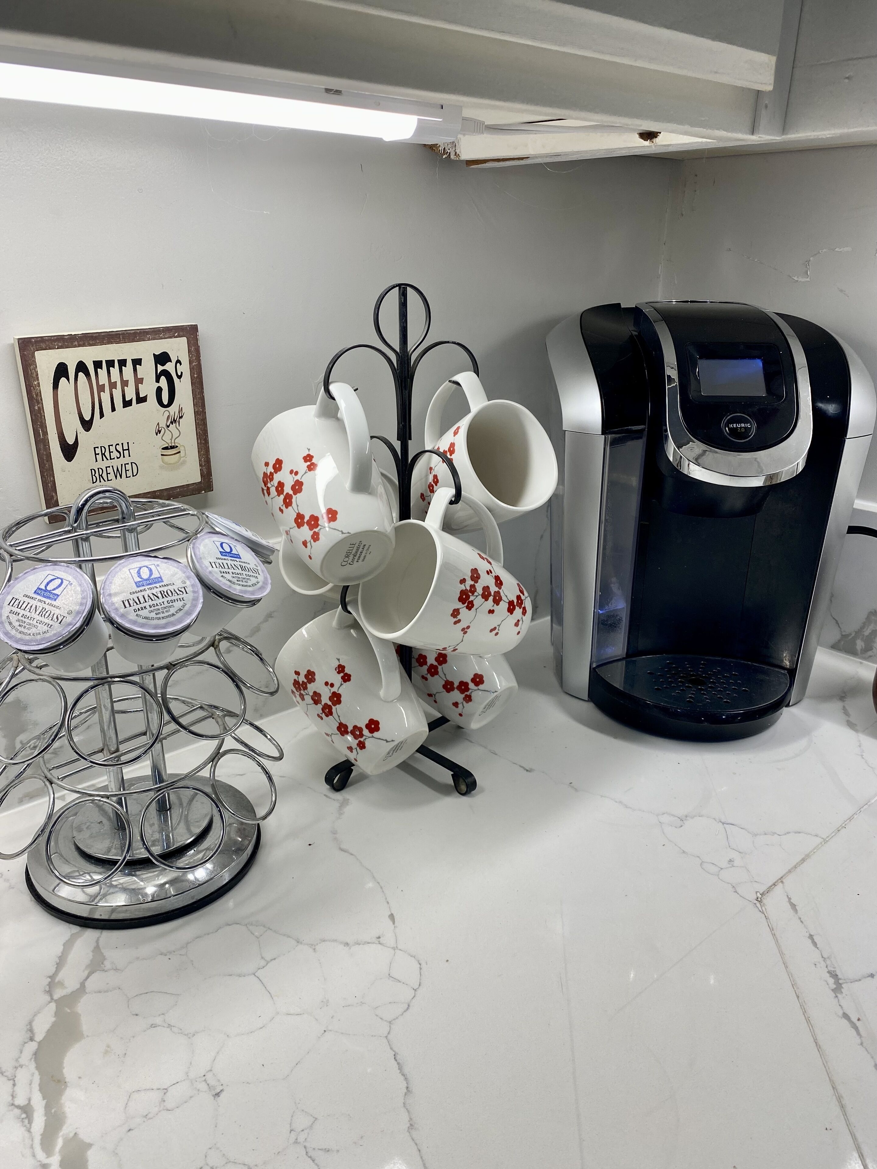 A kitchen counter with a coffee machine, a mug rack with floral mugs, and a coffee sign.