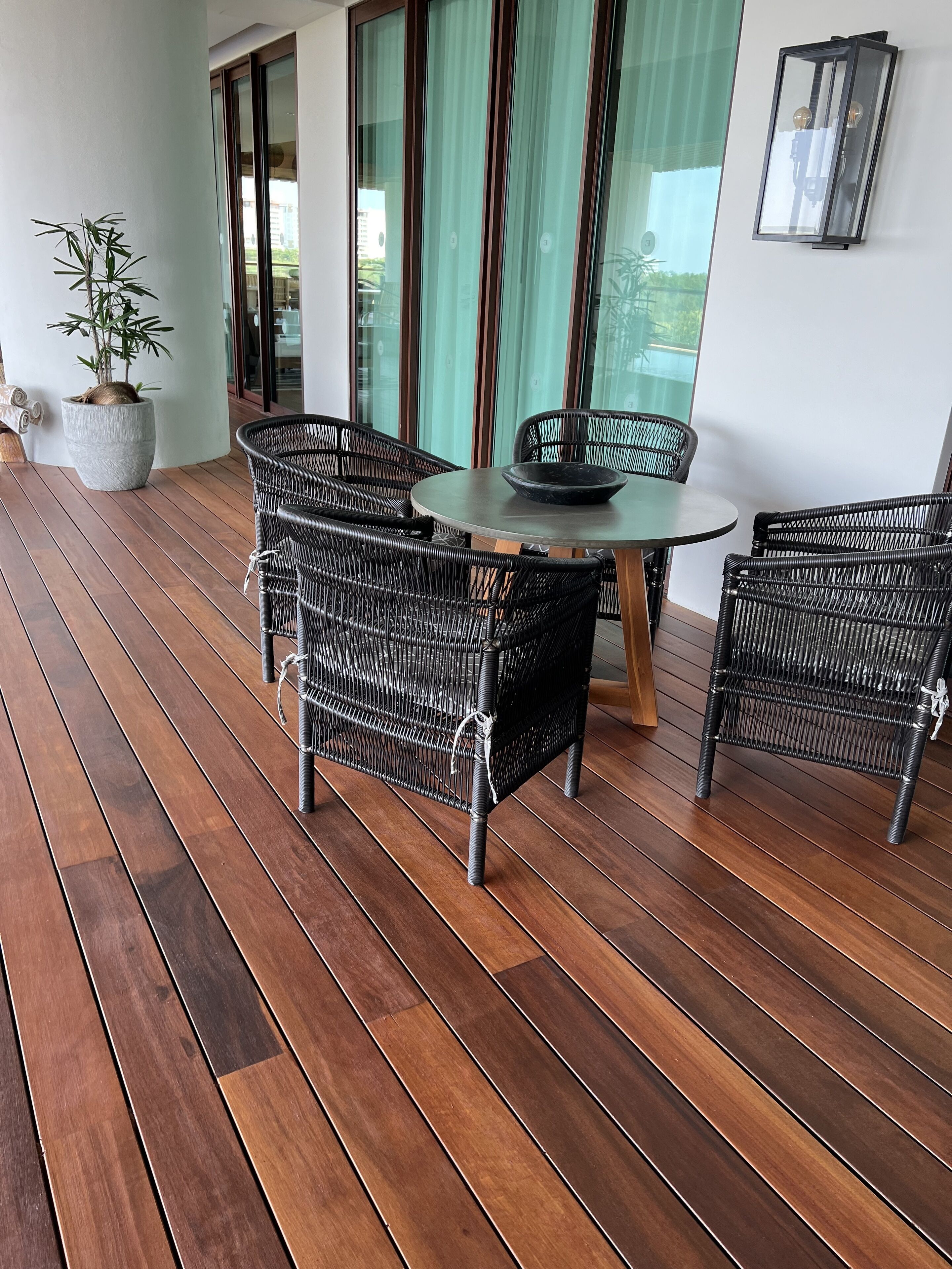 A wooden deck with wicker furniture, a round table, and a potted plant.