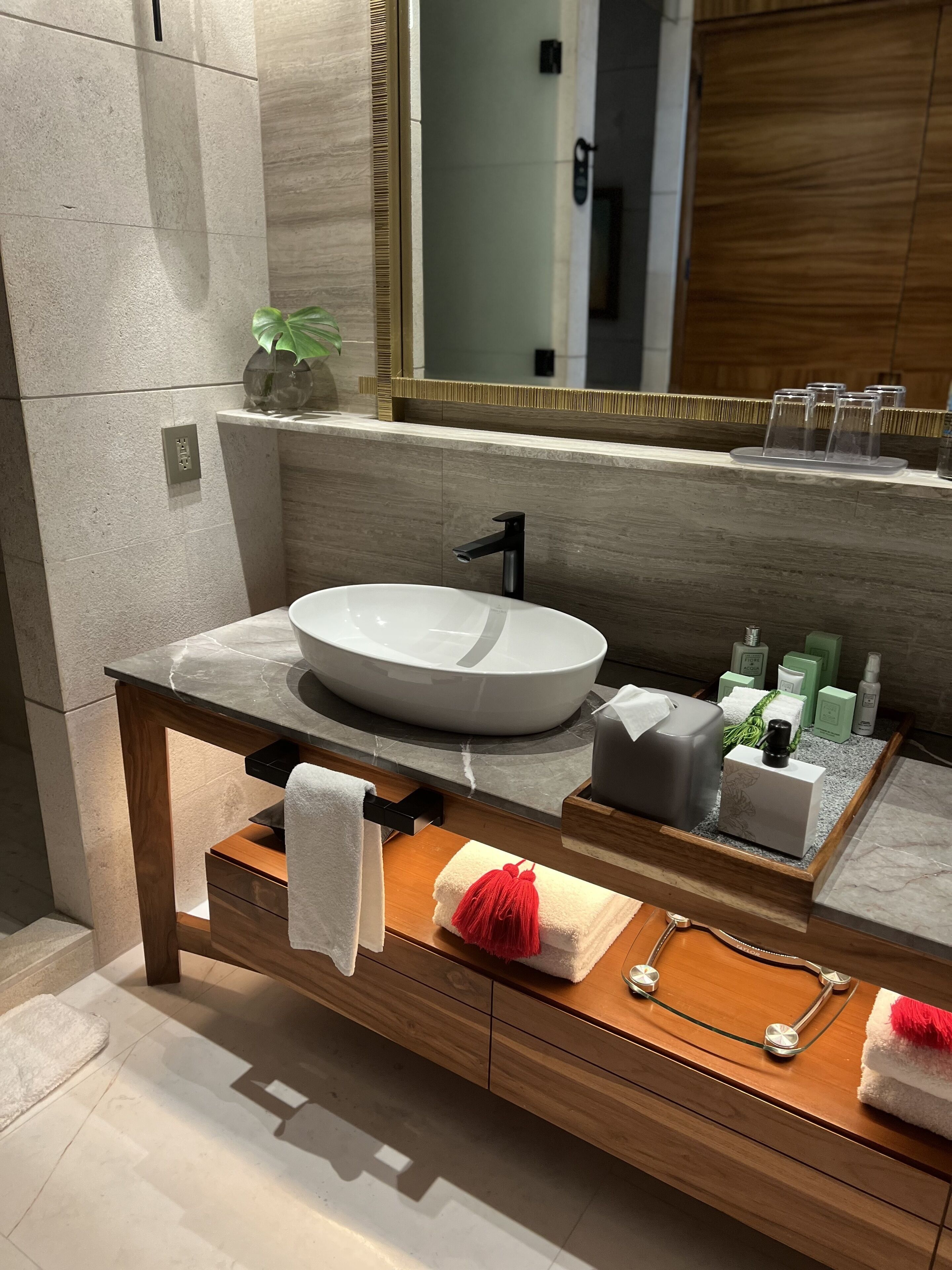 Ein modernes Badezimmer mit einem großen weißen Waschbecken, einem Holzkosmetikschrank und einem Spiegel mit goldener Rahmung.