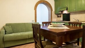 Et hyggeligt køkken med spisebord, stole, en grøn sofa og en murstensbue.