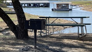 A picnic table and a trash bin near a body of water with a boat dock and buildings in the background. - Village Inn (Breckenridge)