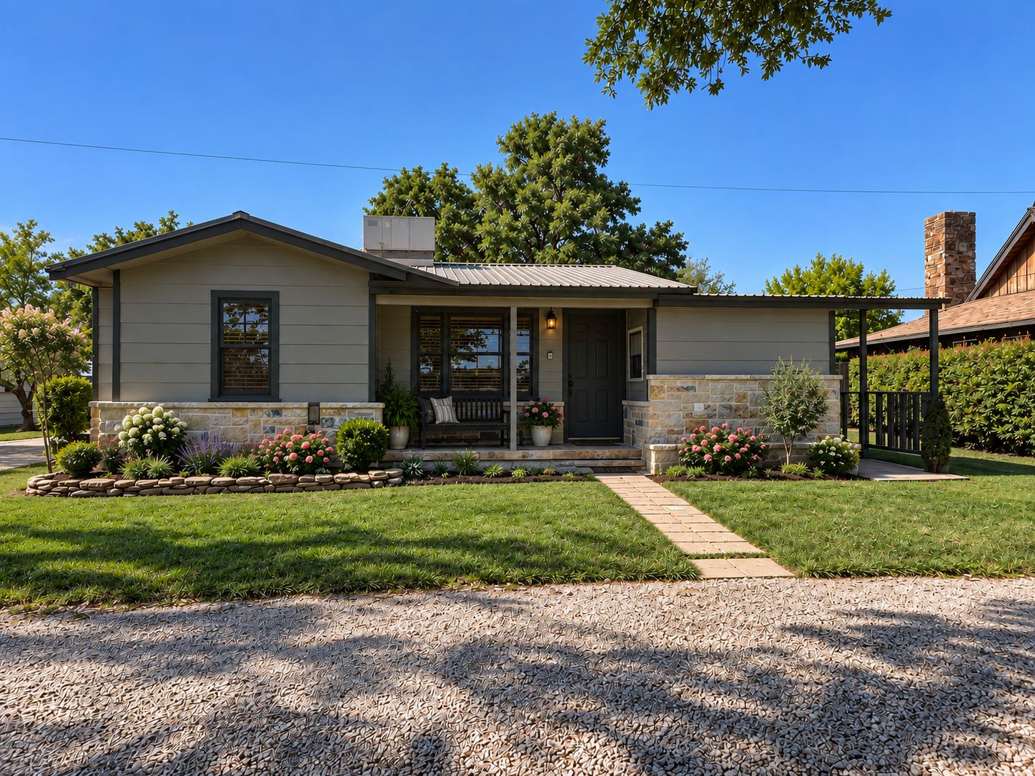 A single-story house with a front porch, a stone foundation, and a gravel driveway.