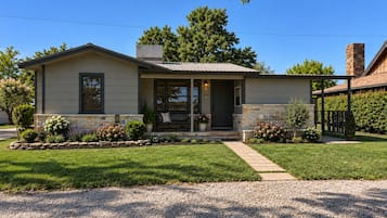 A single-story house with a front porch, a stone foundation, and a gravel driveway.