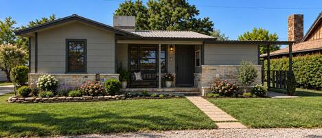 A single-story house with a front porch, a stone foundation, and a gravel driveway.