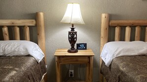 A room with two wooden beds, a wooden nightstand with a lamp, and a digital clock.