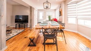 Un vaste espace dédié à la salle à manger, avec une longue table en bois, des chaises noires et un luminaire suspendu au design moderne.