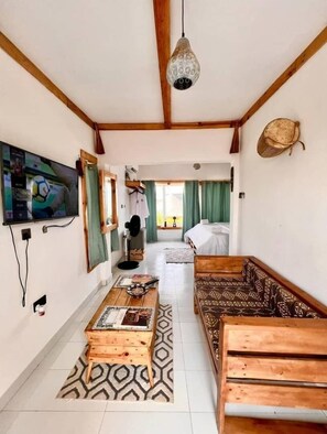 A cozy room with a wooden ceiling, a television on the wall, a bed with green curtains, and a patterned rug.