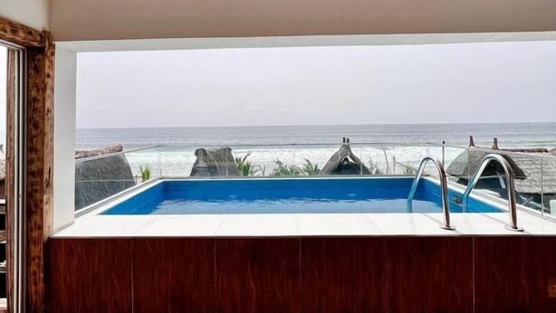 A modern bathroom with a large window overlooking the sea, a built-in bathtub, and a wooden floor. - Lekki Beach Resort- 1 bed & private pool (Lekki)