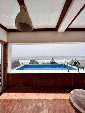 A modern bathroom with a large window overlooking the sea, a built-in bathtub, and a wooden floor.