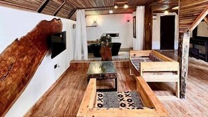 A rustic interior with wooden flooring, a wooden bench with a patterned cushion, and a wall-mounted TV. - Lekki Beach Resort- 1 bed & private pool (Lekki)