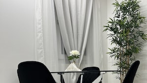 A dining area with a glass table surrounded by black chairs with gold legs.