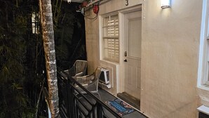 A building with a beige exterior, a door with a window, and a small porch area with chairs and a mat. - Sirena Azul SoBe Suite 3 (Miami Beach)