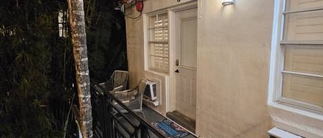 Un bâtiment à l’extérieur beige, avec une porte dotée d’une fenêtre et un petit porche aménagé avec des chaises et un tapis.