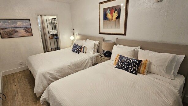 A hotel room with two beds, a wardrobe, a TV, and artwork on the walls. - Sirena Azul SoBe Suite 3 (Miami Beach)