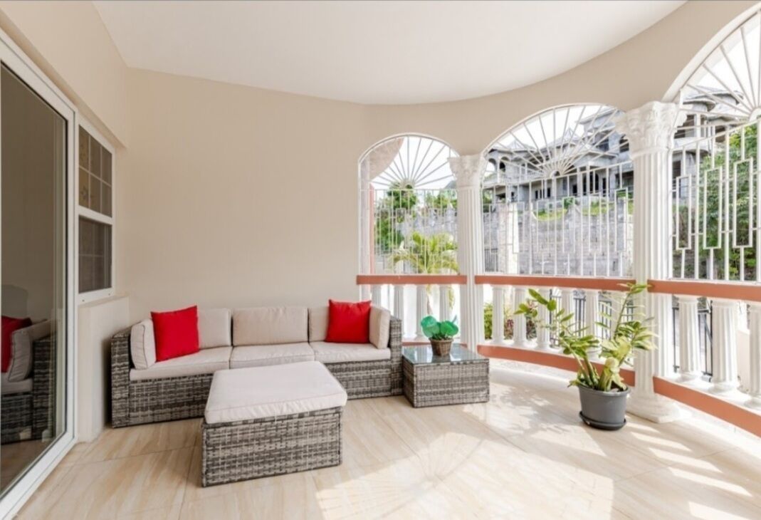 Een zonnige kamer met een rieten bank, een klein voetenbankje en een potplant.
