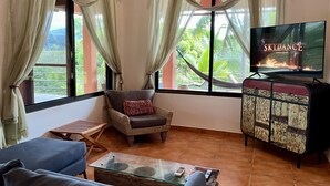 Uma sala de estar com televisão, sofá, poltrona e mesa de centro de vidro.
