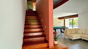 A wooden staircase leading to an upper floor, a beige sofa, and a pool table in a modern living area. - Quinta Trindade (Arouca)