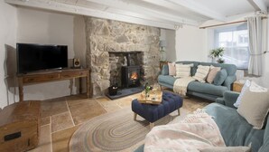 Ein gemütliches Wohnzimmer mit Kamin aus Stein, einem Fernseher, einer Couch und einem Couchtisch.
