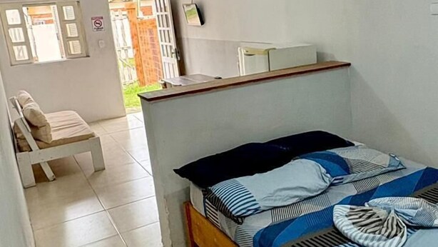 Habitació petita i senzilla amb un llit individual, una cadira i una taula.