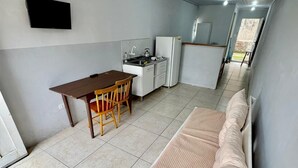 Habitació petita i senzilla amb llit, escriptori, cadira i cuina americana.