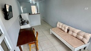 Habitació petita i senzilla amb llit, taula i cadires. Disposa d'un petit espai de cuina amb un rentamiques i un mirall.