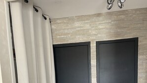 Una habitación con dos puertas negras, suelo de madera y una pared de color claro con textura.