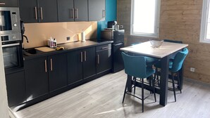 Una cocina moderna con armarios negros, encimera de madera y un comedor con sillas azules.