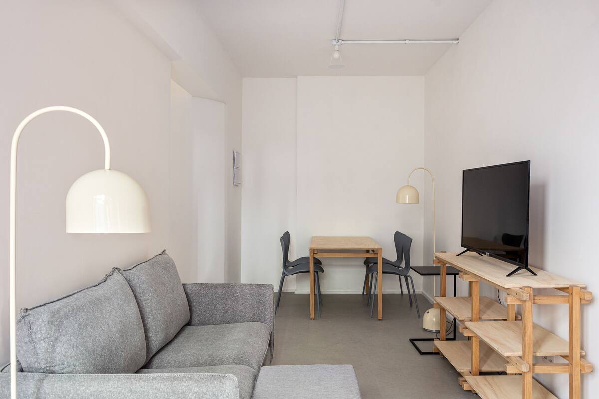 A modern living room with a grey sofa, a wooden TV stand, and a dining area with a table and chairs.