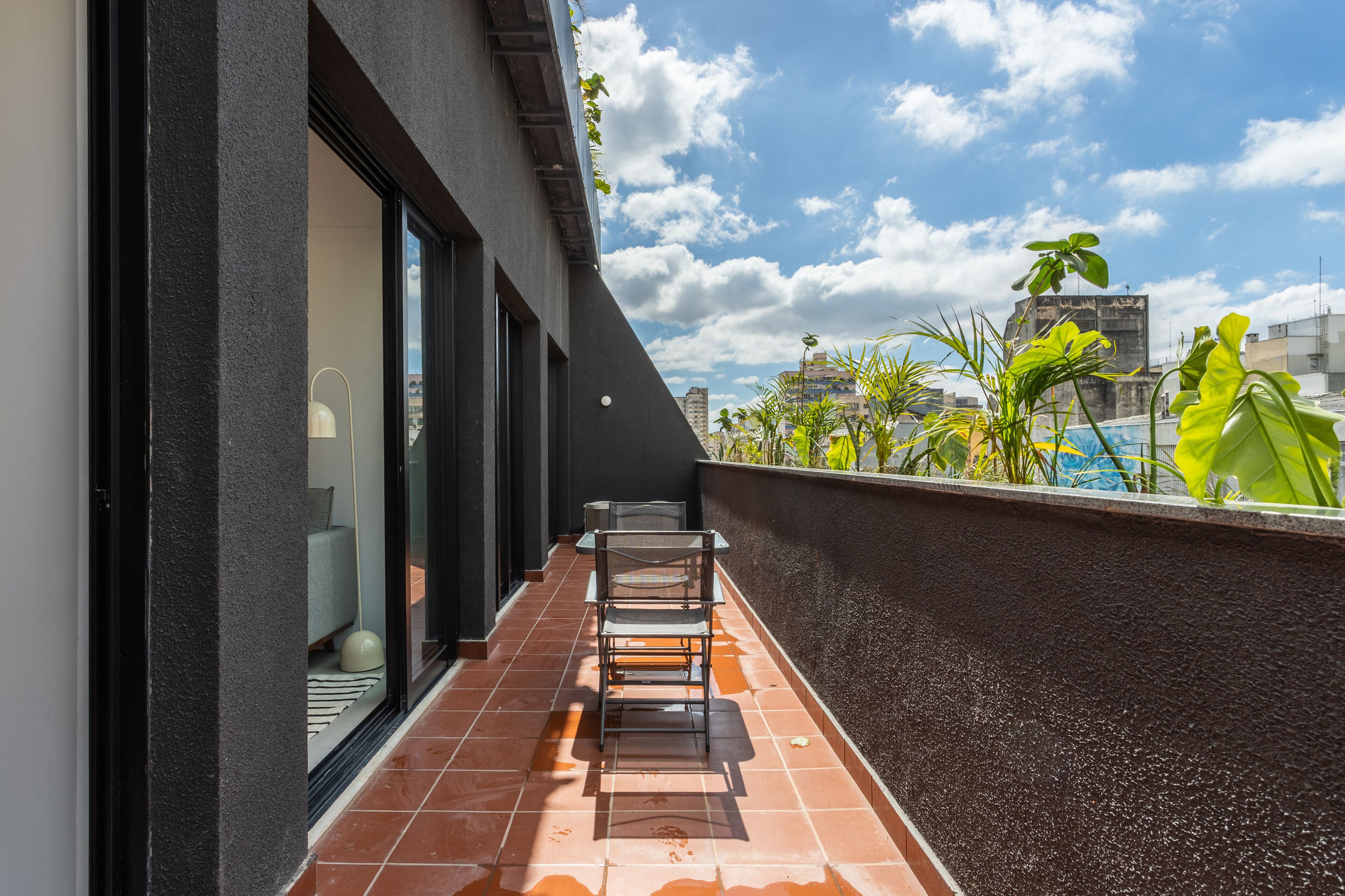 A modern balcony with a tiled floor, a glass door, and a metal railing.