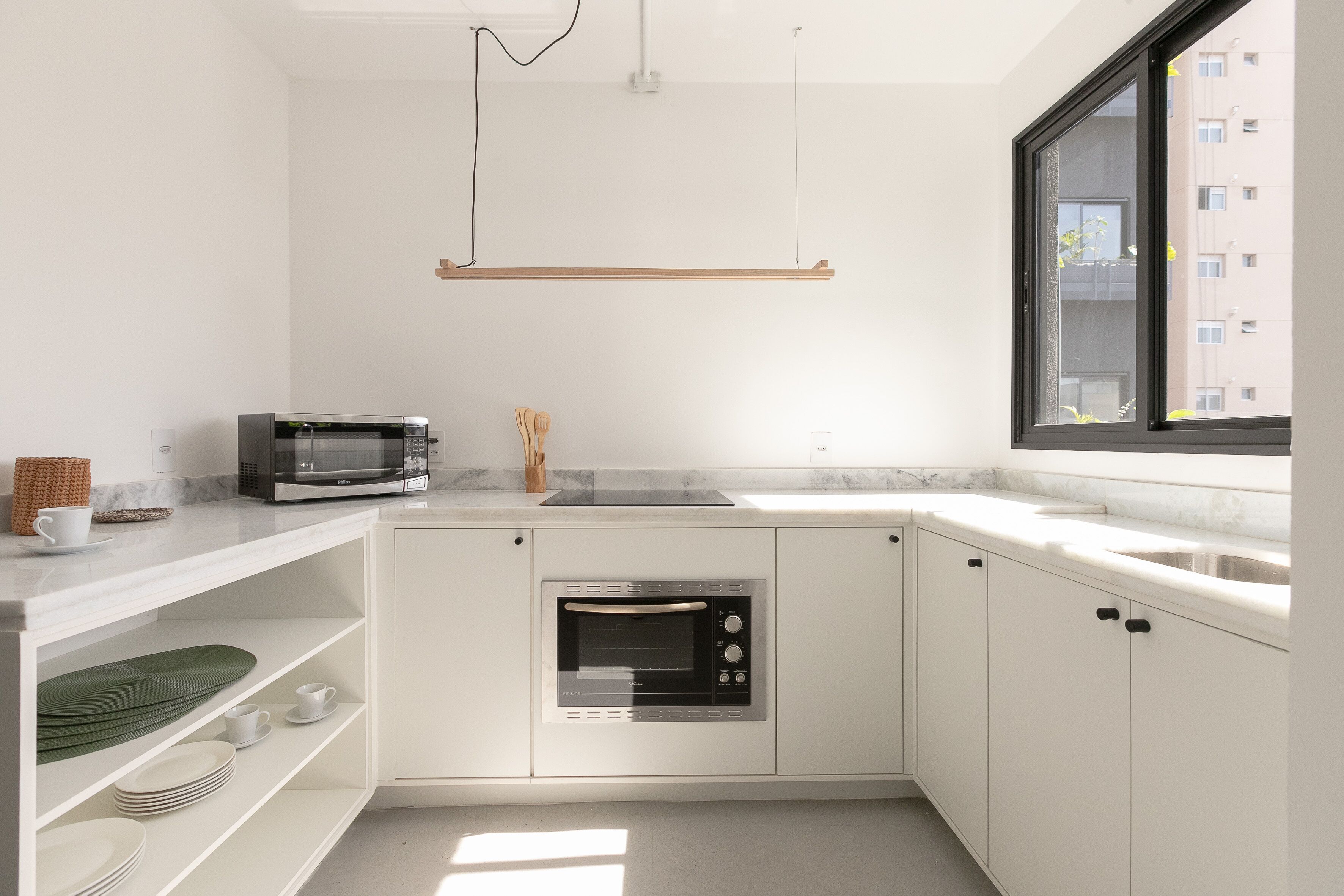 Une cuisine moderne avec des meubles blancs, un four encastré, un four à micro-ondes et une fenêtre donnant sur un bâtiment à l’extérieur.