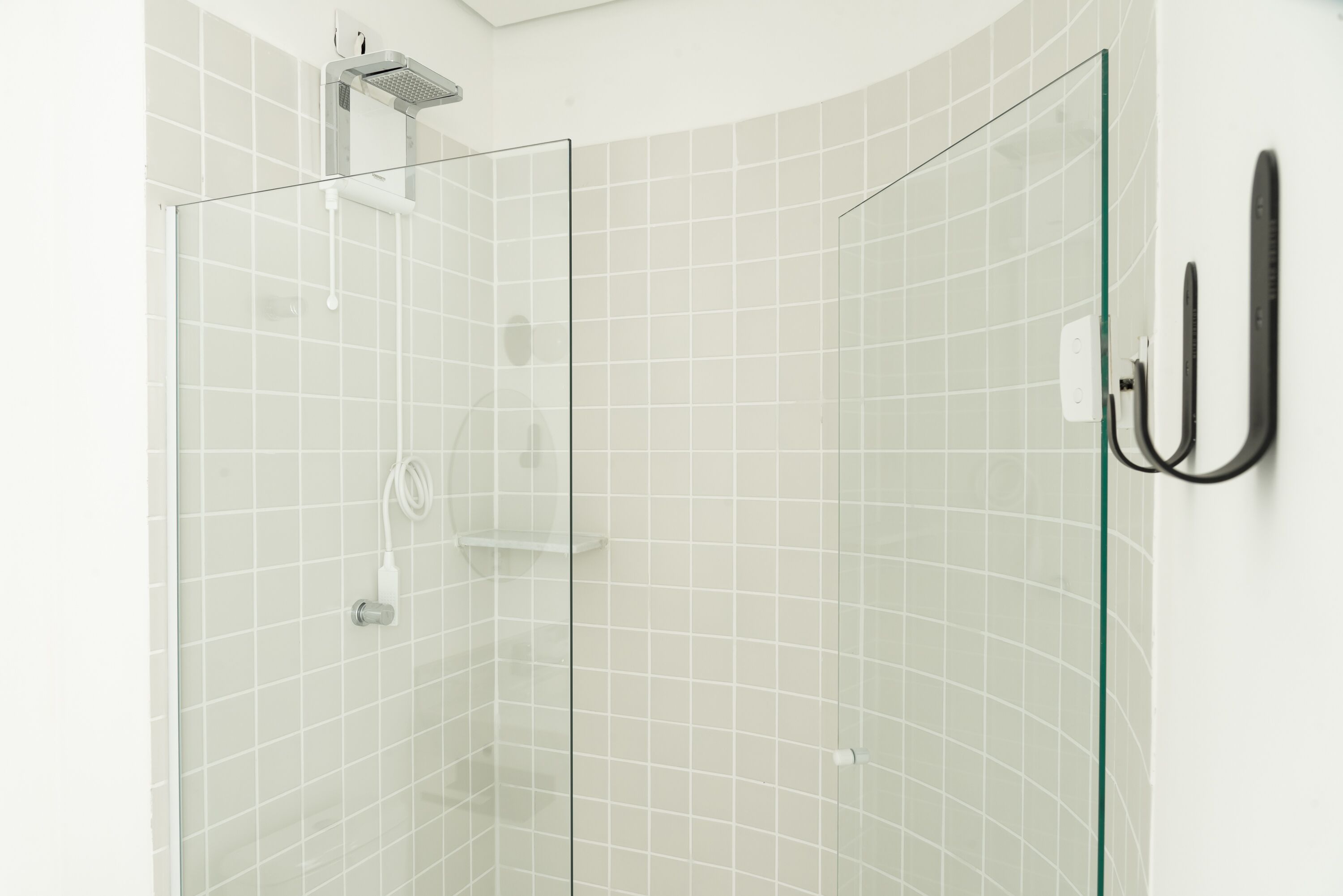 Una ducha con paredes de vidrio, pared de azulejos blancos y un perchero negro.