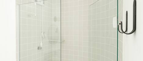 Una ducha con paredes de vidrio, pared de azulejos blancos y un perchero negro.