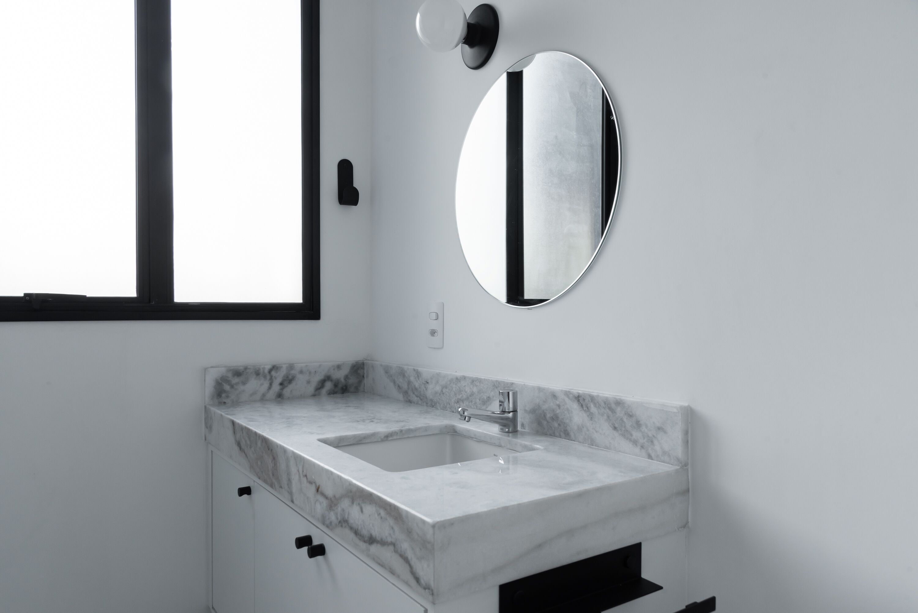 Une salle de bain moderne avec un lavabo en marbre, un miroir rond et une fenêtre.