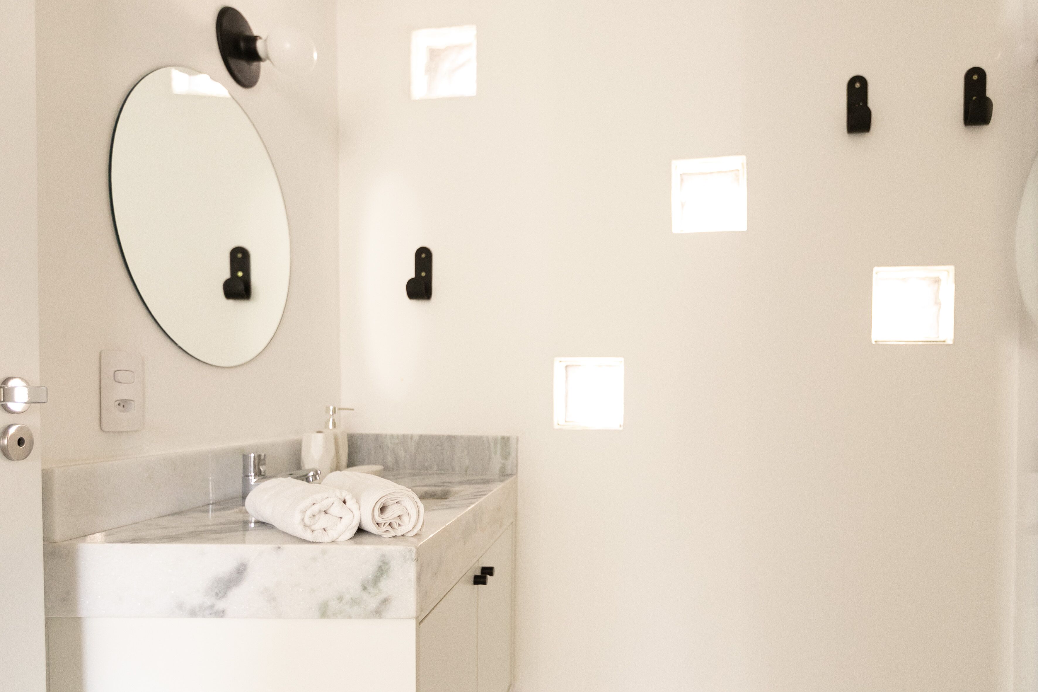A modern bathroom with a marble countertop, a large oval mirror, and multiple wall-mounted light switches.