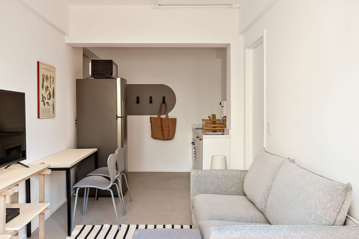 A compact living space with a kitchenette, a sofa, a dining area with chairs, and a television.