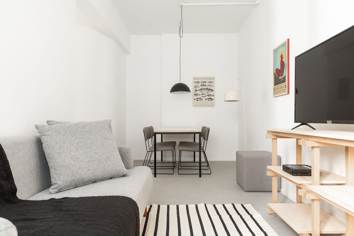 A modern, minimalist room with a sofa, a dining table with chairs, a TV, and a small rug.