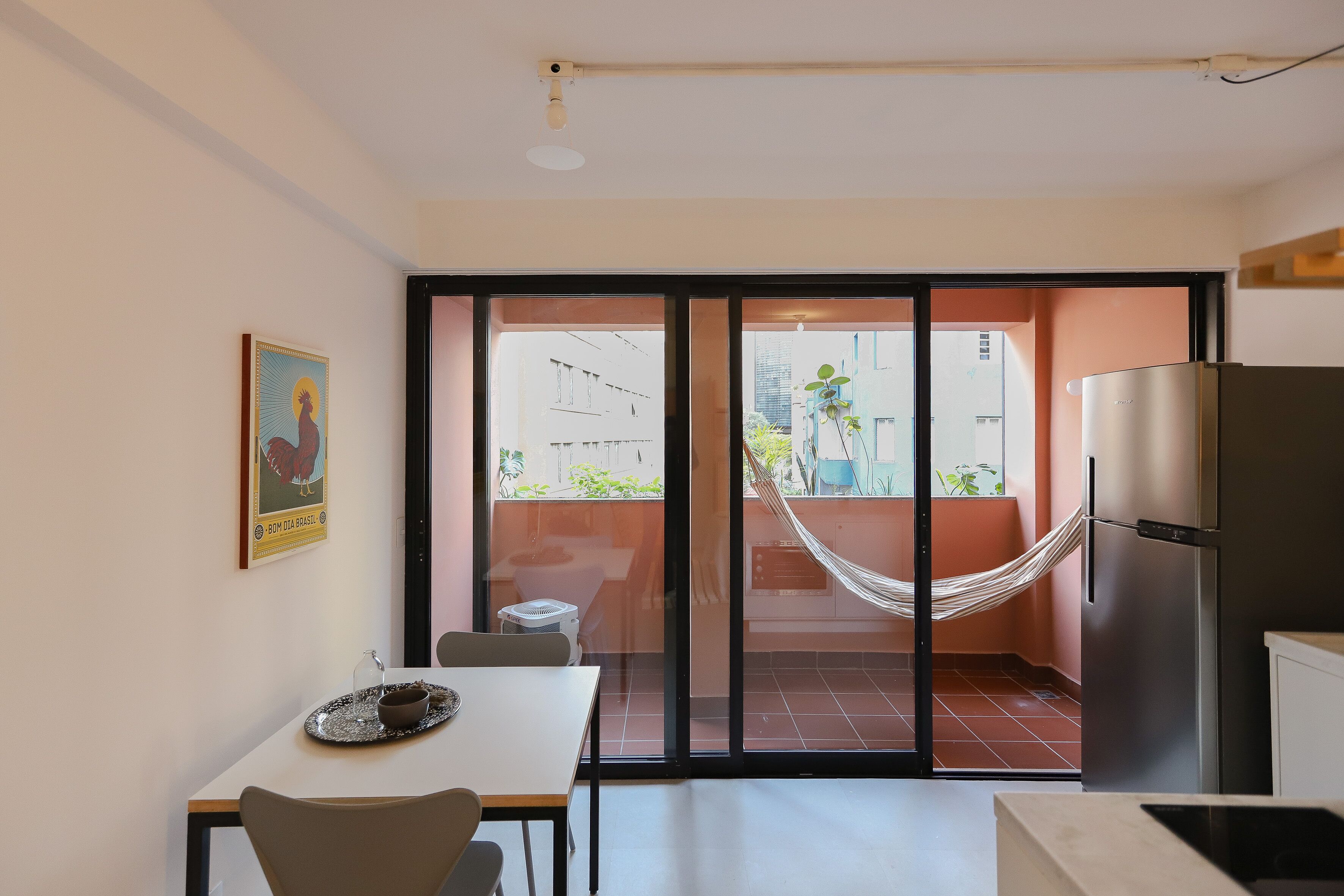 A modern kitchen with a refrigerator, a dining table with chairs, and a sliding glass door leading to a balcony with a hammock.