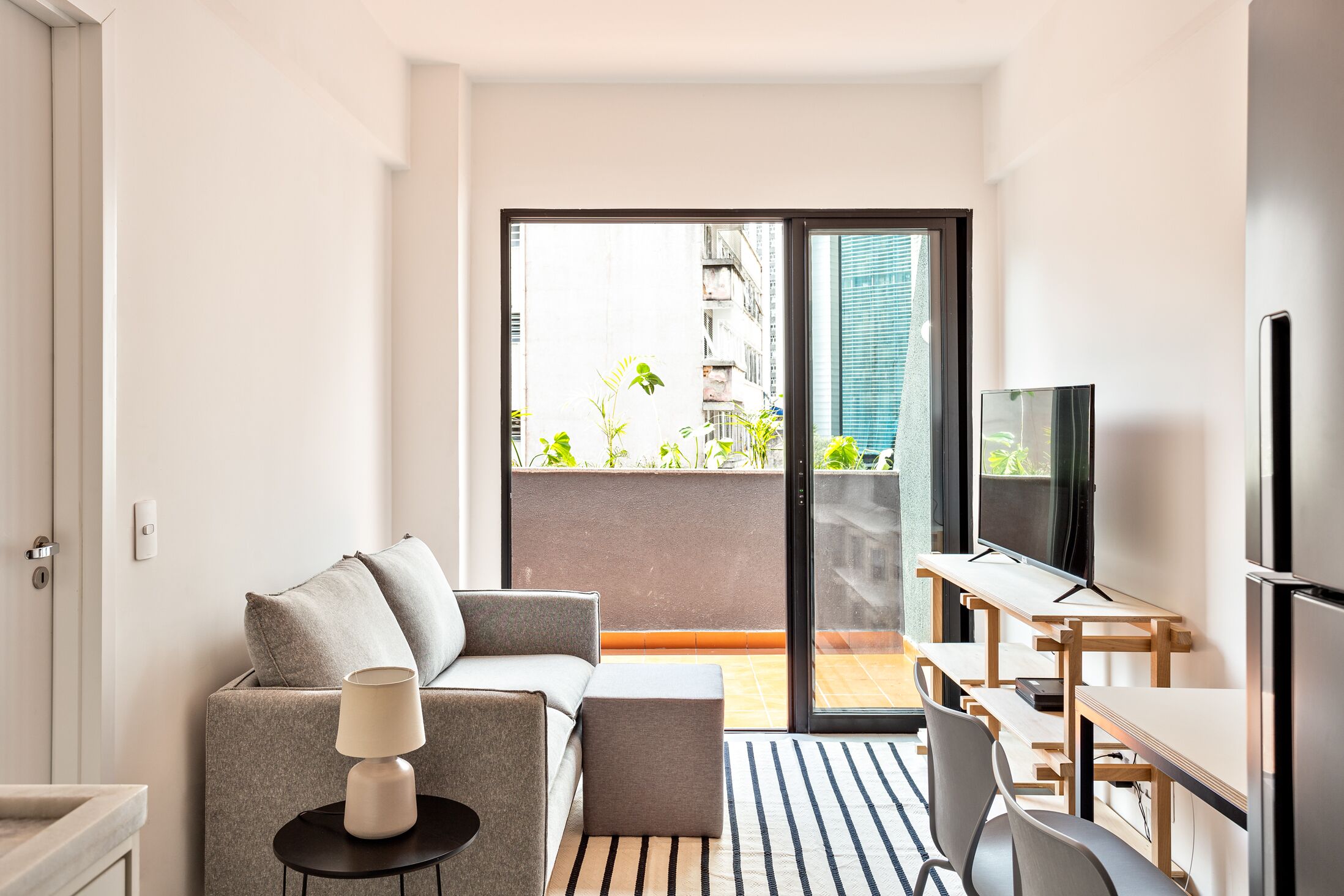 A modern living room with a sofa, a small table, a TV, and a balcony with plants.