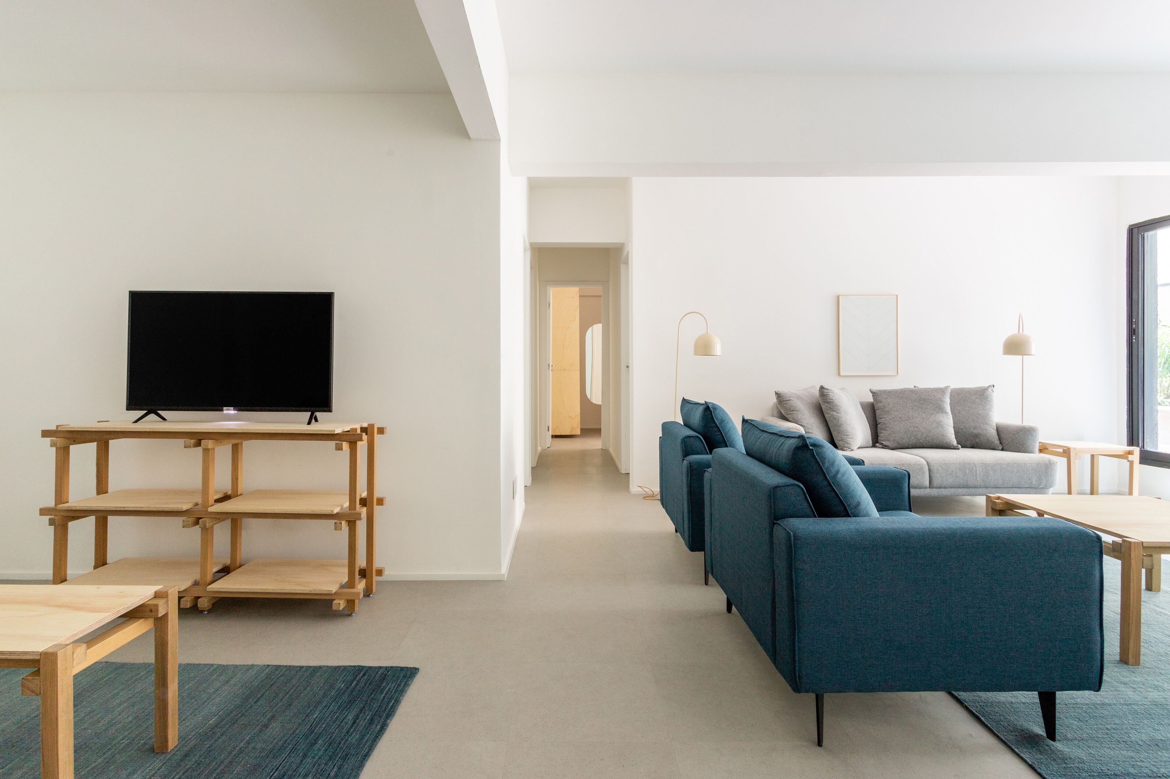 A modern living room with a TV on a wooden stand, a blue sofa, a grey couch, and a wooden coffee table.