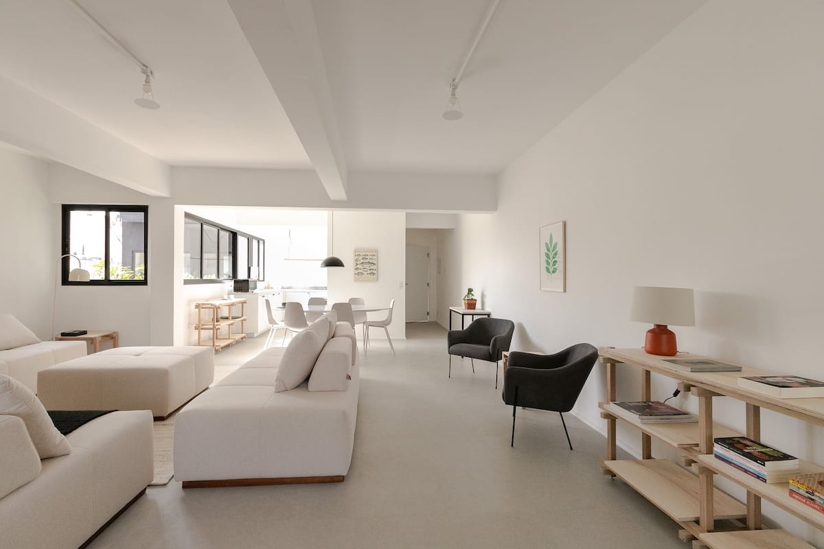A modern living room with a white sofa, a black armchair, and a wooden side table with books.
