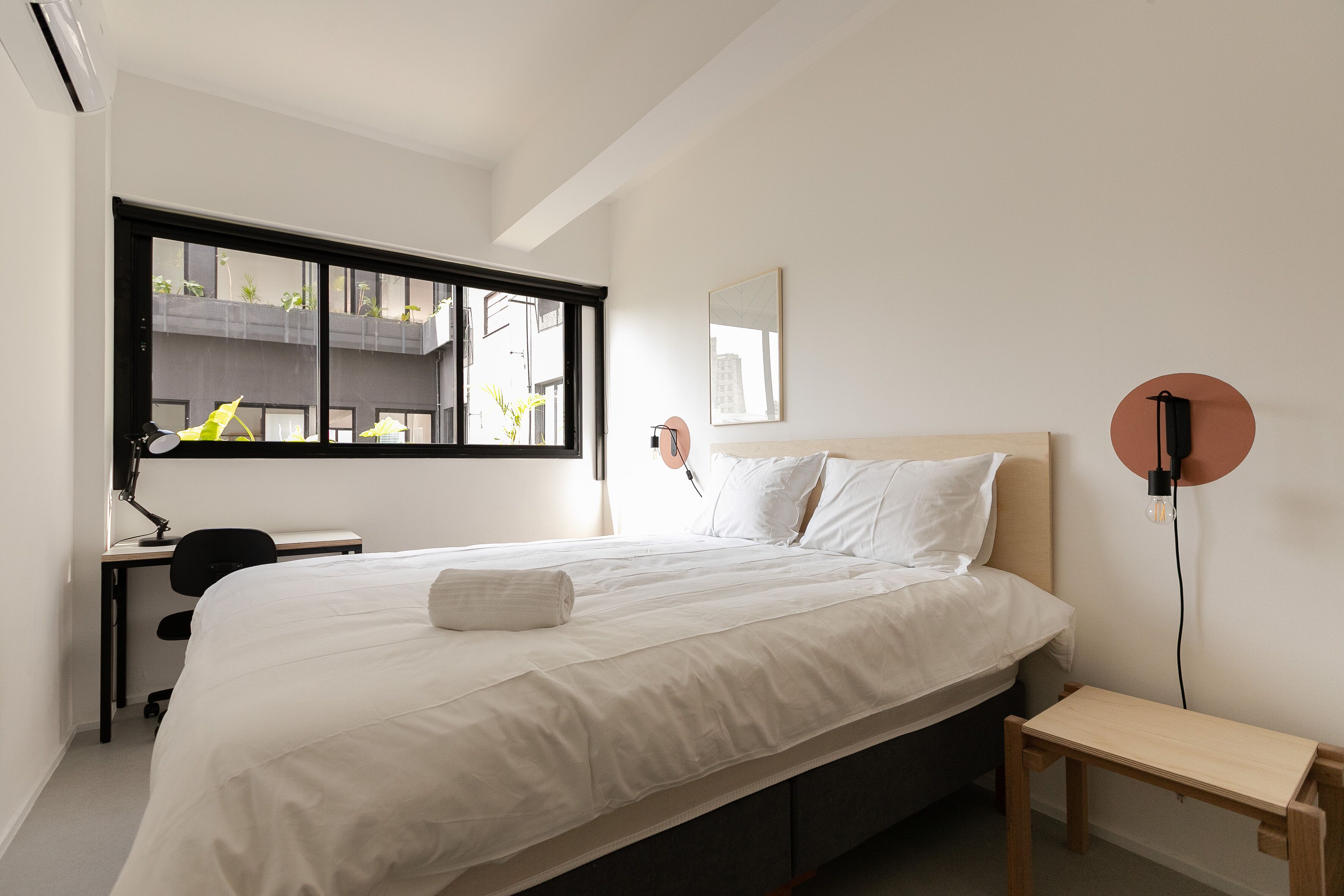 Een moderne hotelkamer met een groot bed, een bureau en een raam met uitzicht op gebouwen.