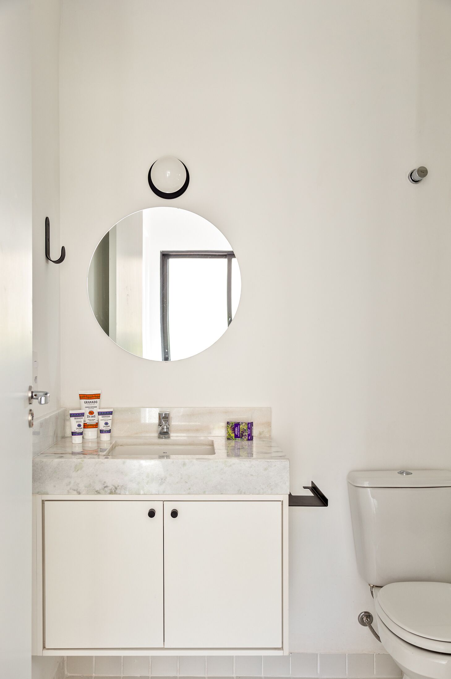 A bathroom with a white sink, mirror, and toilet. There are toiletries on the sink.