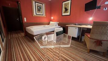 Quarto de hotel com cama, escrivaninha, cadeira, pequeno kitchenette e placa indicando que o quarto está pronto para hóspedes.