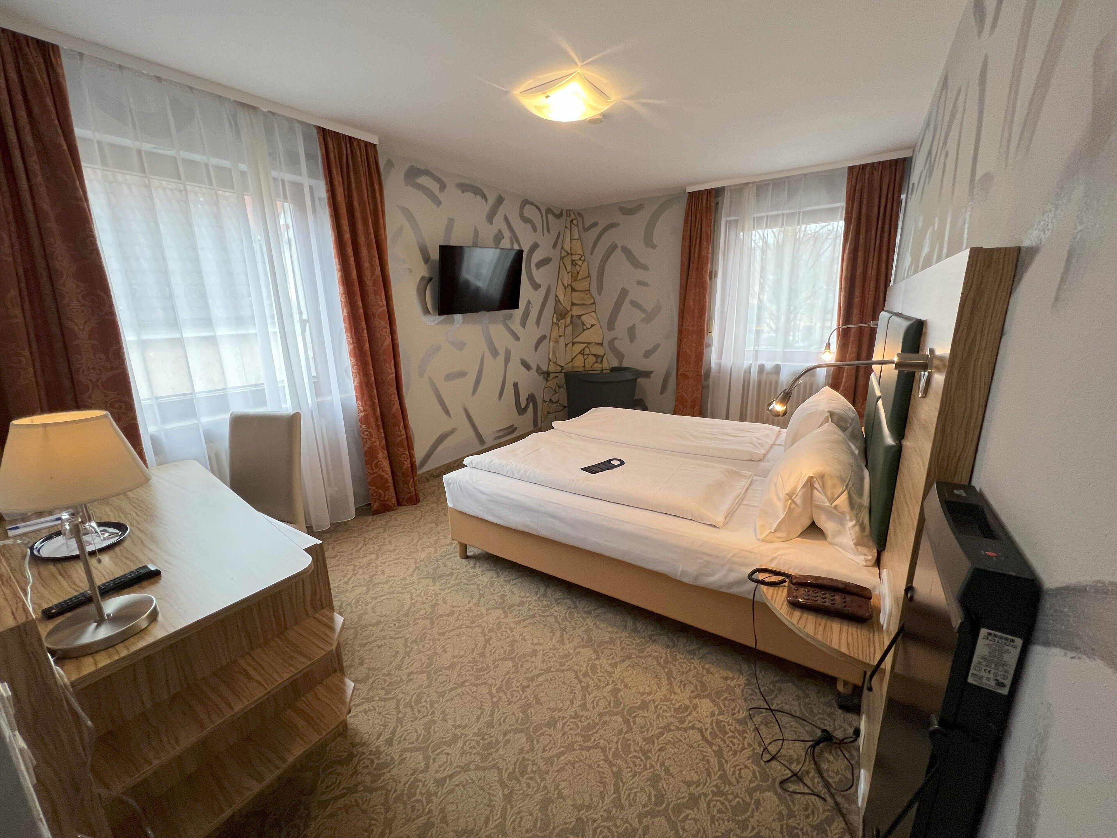A hotel room with a bed, a desk, a chair, a TV, and a mirror.