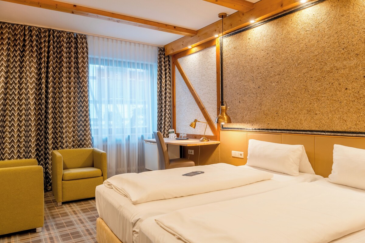 A hotel room with a bed, two yellow armchairs, a desk, and a mirror.